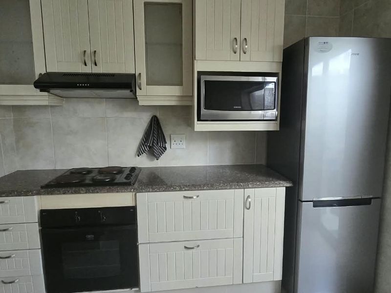 A functional kitchen featuring cream-colored cabinetry, granite countertops, a built-in oven, hob, extractor fan, and integrated microwave with tiled wall finishes.