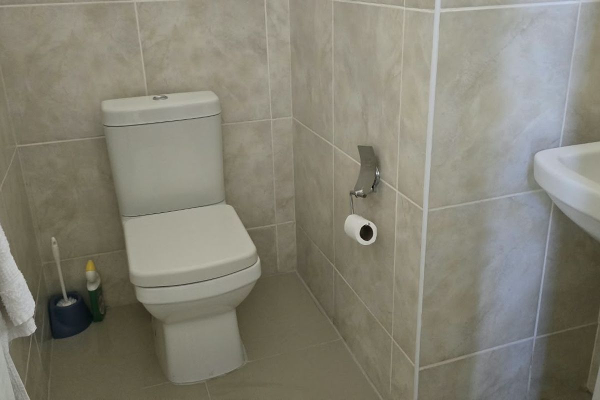 A compact bathroom featuring a modern toilet and a pedestal basin, finished with neutral ceramic wall and floor tiles.