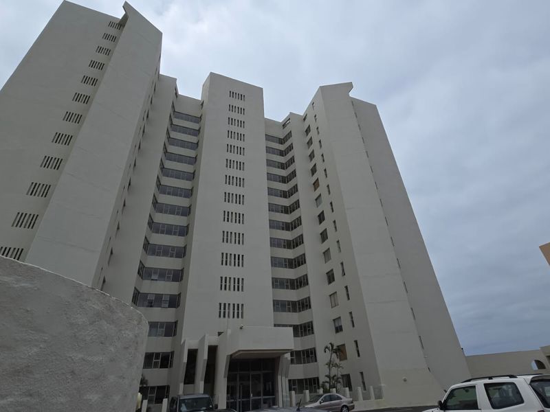 A low-angle view of a multi-story apartment building facade featuring a prominent entrance canopy and numerous windows under an overcast sky.
