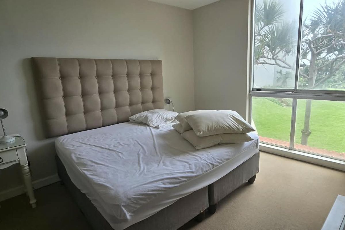 A bedroom featuring neutral walls, carpeted flooring, and a large window providing natural light and garden views.