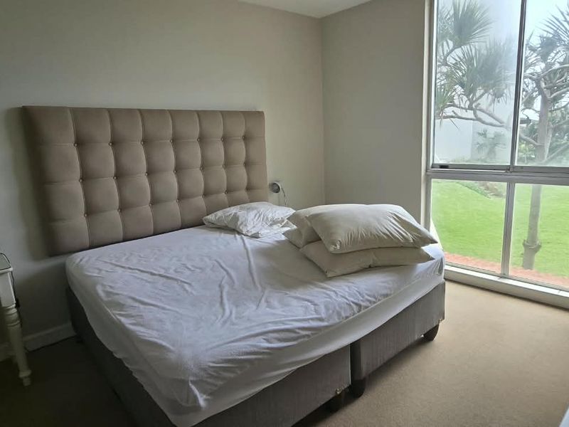 A bedroom featuring neutral walls, carpeted flooring, and a large window providing natural light and garden views.