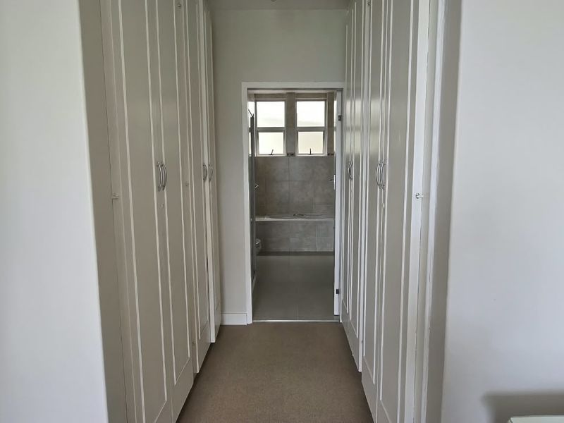 A hallway featuring extensive built-in cupboard storage, leading directly into a tiled bathroom area.