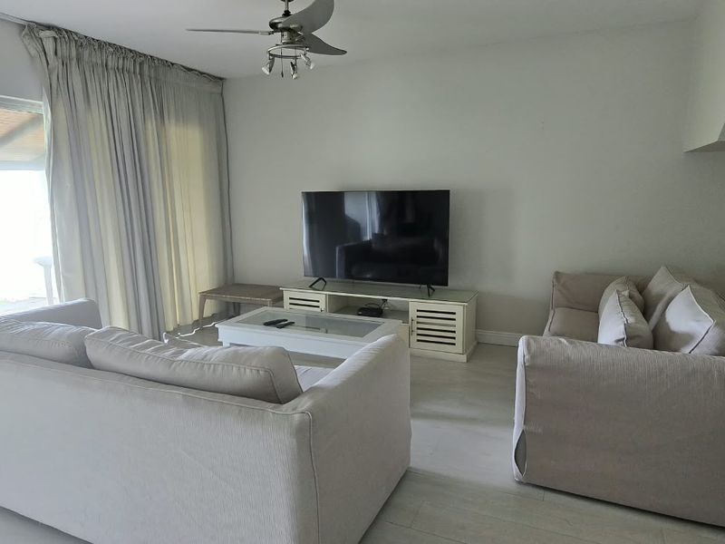 A comfortable living room featuring light-toned laminate flooring, a ceiling fan, and large sliding glass doors that provide access to the outdoor area.