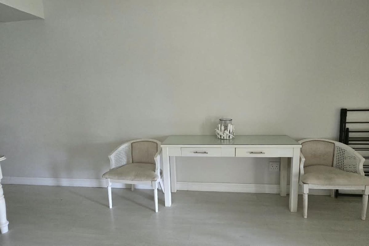 A neutrally painted living area featuring light-toned flooring, skirting boards, and a visible electrical outlet, offering a blank canvas for interior design.