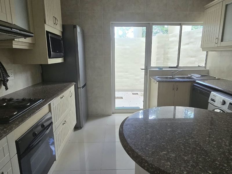 Functional kitchen featuring granite countertops, built-in cabinetry, electric hob, oven, and direct access to an outdoor area through a glass door.