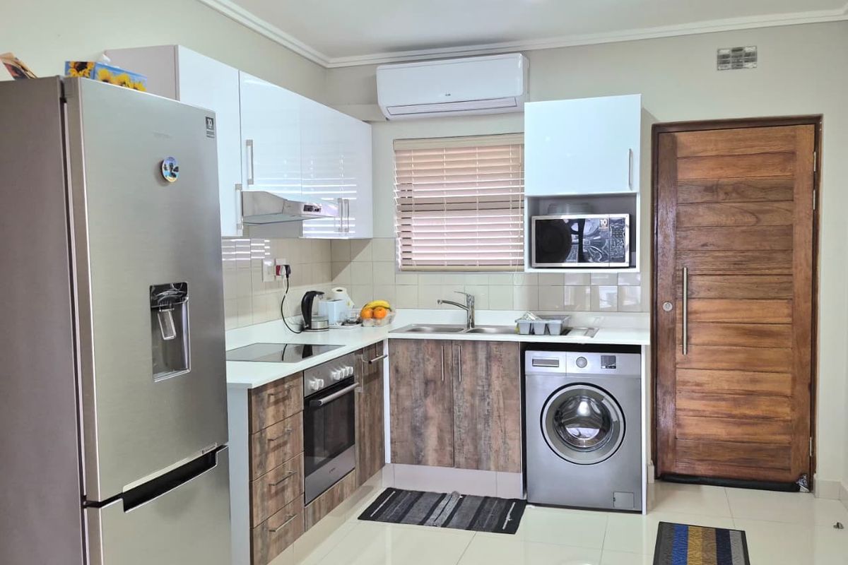 Modern kitchen featuring two-tone cabinetry, integrated appliances, tiled flooring, and a solid timber entrance door, providing a functional and well-maintained cooking space.
