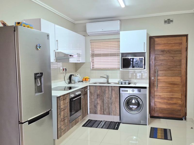 Modern kitchen featuring two-tone cabinetry, integrated appliances, tiled flooring, and a solid timber entrance door, providing a functional and well-maintained cooking space.