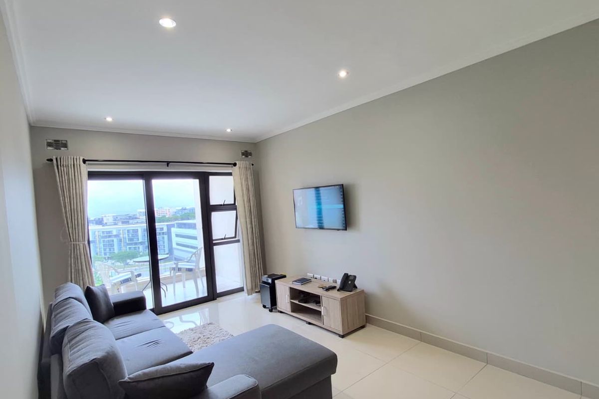 A bright and modern living room featuring neutral tiled flooring, recessed downlighting, and large sliding glass doors leading to an outdoor balcony area.
