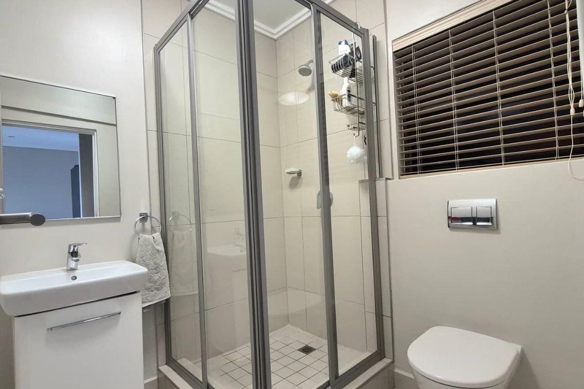 A modern, well-maintained bathroom featuring a glass shower enclosure, wall-hung toilet, and a sleek vanity basin with neutral tiling throughout.