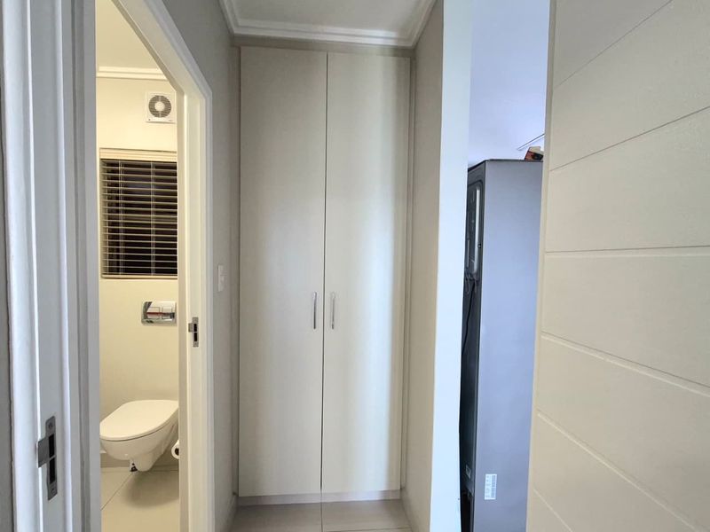 A clean, well-maintained hallway featuring neutral tiled flooring, built-in storage cupboards, and direct access to an adjacent bathroom.
