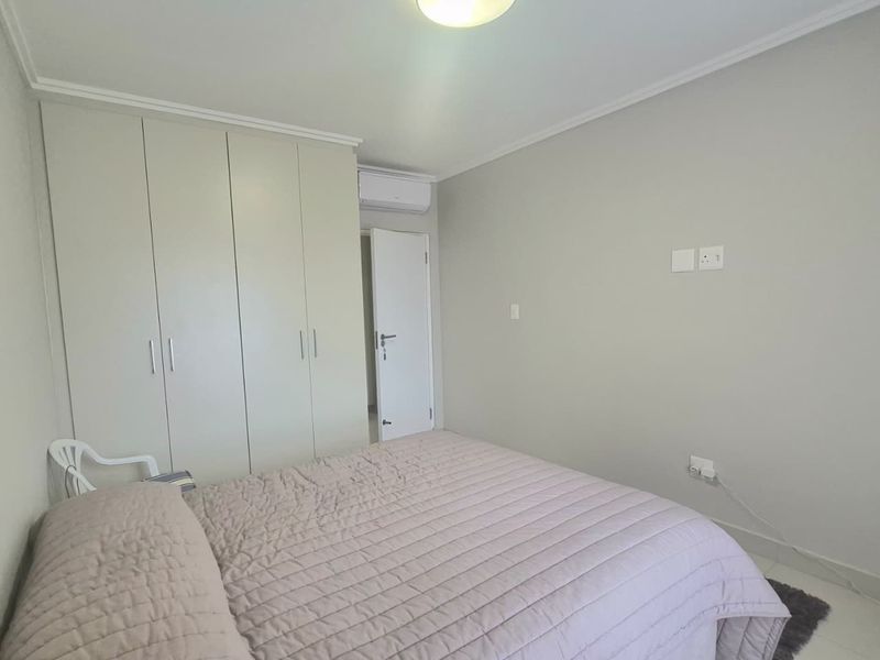 A clean, neutral bedroom featuring built-in cupboards, an air conditioning unit, and tiled flooring, offering a functional and well-maintained living space.