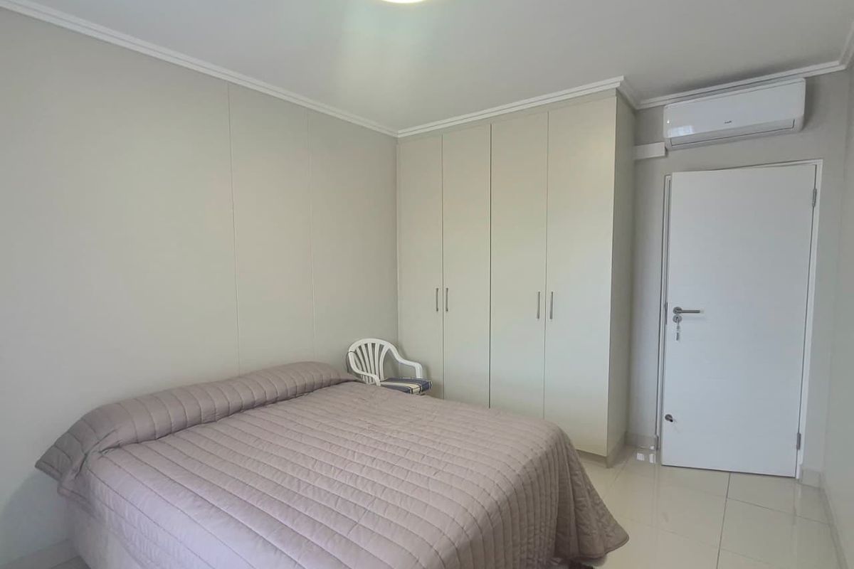 A clean bedroom featuring built-in cupboards, tiled flooring, and a wall-mounted air conditioning unit.