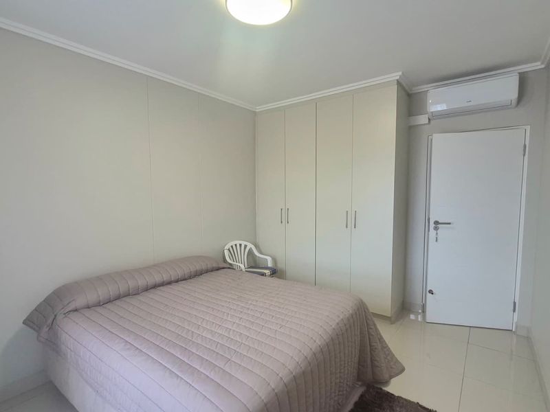 A clean bedroom featuring built-in cupboards, tiled flooring, and a wall-mounted air conditioning unit.