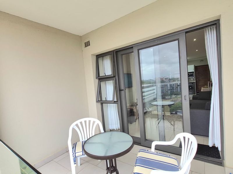 A covered balcony featuring tiled flooring, a glass balustrade, and large sliding glass doors providing access to the interior living space.