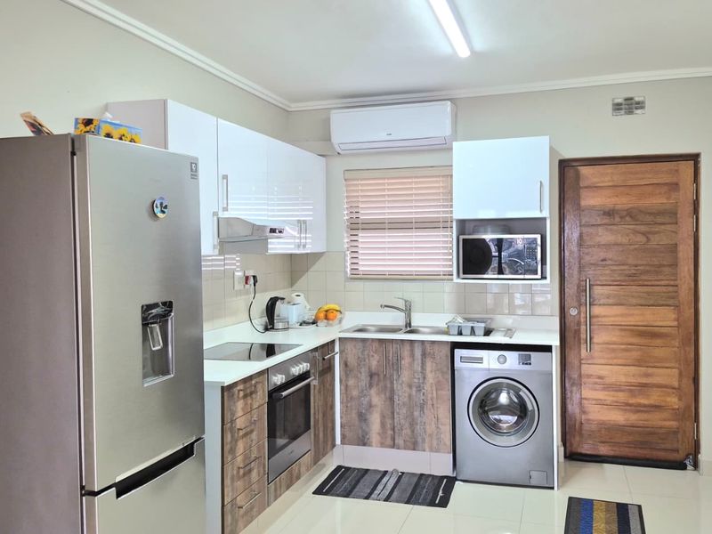 Modern kitchen featuring two-tone cabinetry, built-in oven and hob, integrated washing machine, and tiled flooring with an air conditioning unit.