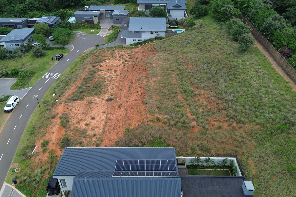 Aerial view of a vacant residential plot featuring sloped terrain and perimeter fencing within a developed estate.