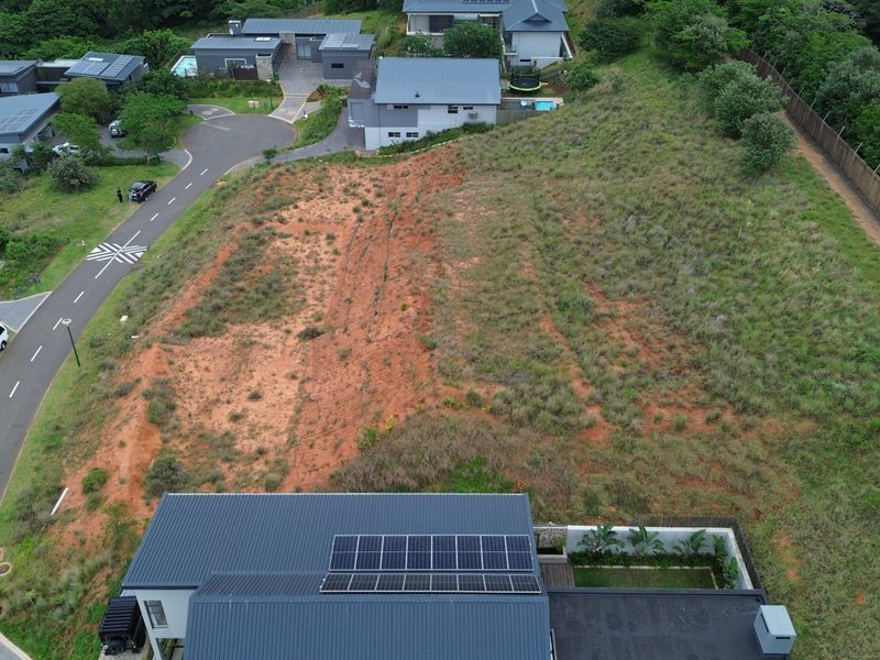 Aerial view of a vacant residential plot featuring sloped terrain and perimeter fencing within a developed estate.