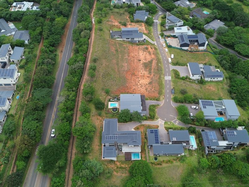 Aerial view of a vacant residential plot situated within a developed estate, surrounded by established modern homes and paved access roads.
