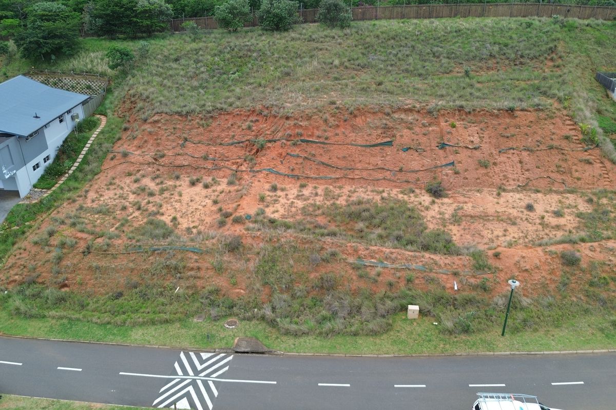 Aerial view of a vacant residential plot featuring sloped terrain with existing erosion control measures, situated in a developed neighborhood.