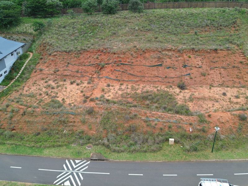 Aerial view of a vacant residential plot featuring sloped terrain with existing erosion control measures, situated in a developed neighborhood.