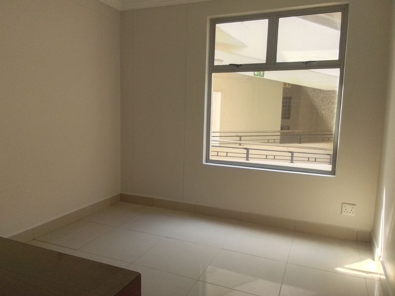 A bright, empty bedroom featuring neutral tiled flooring and a large aluminium-framed window, providing a clean and versatile space ready for furnishing.