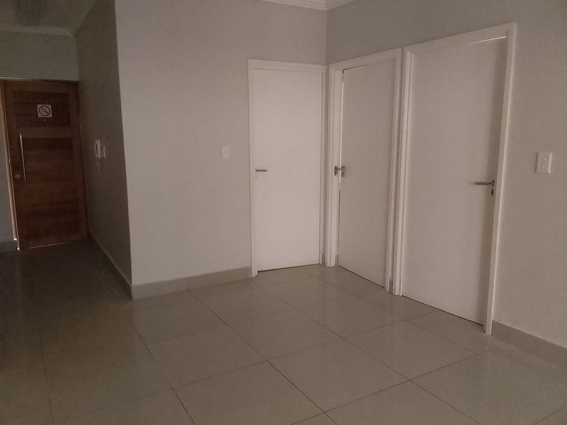 A clean and neutral hallway featuring tiled flooring and multiple internal doors, providing access to various rooms within the apartment.