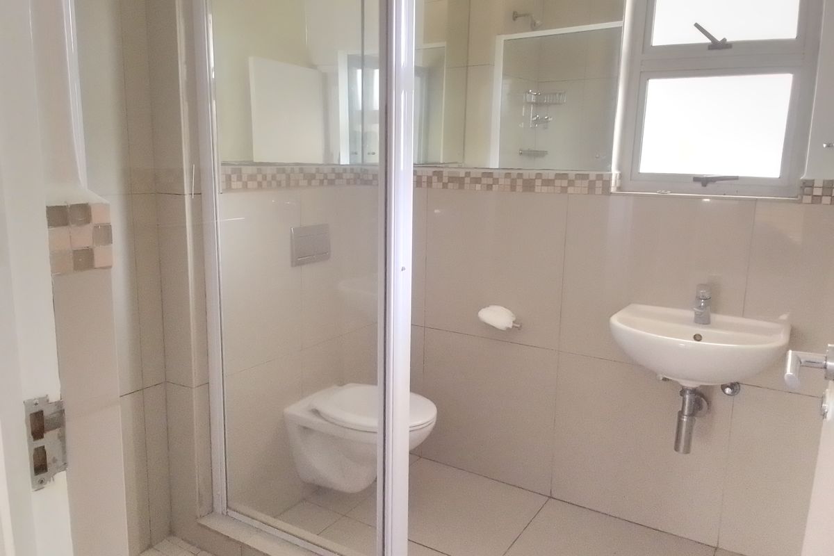 A clean, modern bathroom featuring a wall-mounted toilet, glass shower enclosure, and wall-mounted basin with neutral tiled finishes.
