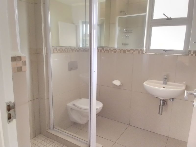 A clean, modern bathroom featuring a wall-mounted toilet, glass shower enclosure, and wall-mounted basin with neutral tiled finishes.