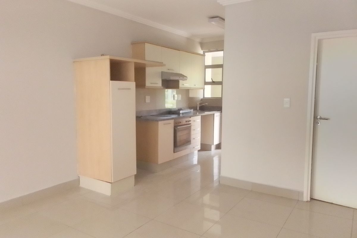 A clean, empty kitchen featuring light-toned built-in cabinetry, tiled flooring, and integrated appliances, offering a functional and neutral space ready for personalization.