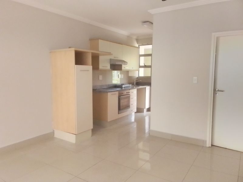 A clean, empty kitchen featuring light-toned built-in cabinetry, tiled flooring, and integrated appliances, offering a functional and neutral space ready for personalization.