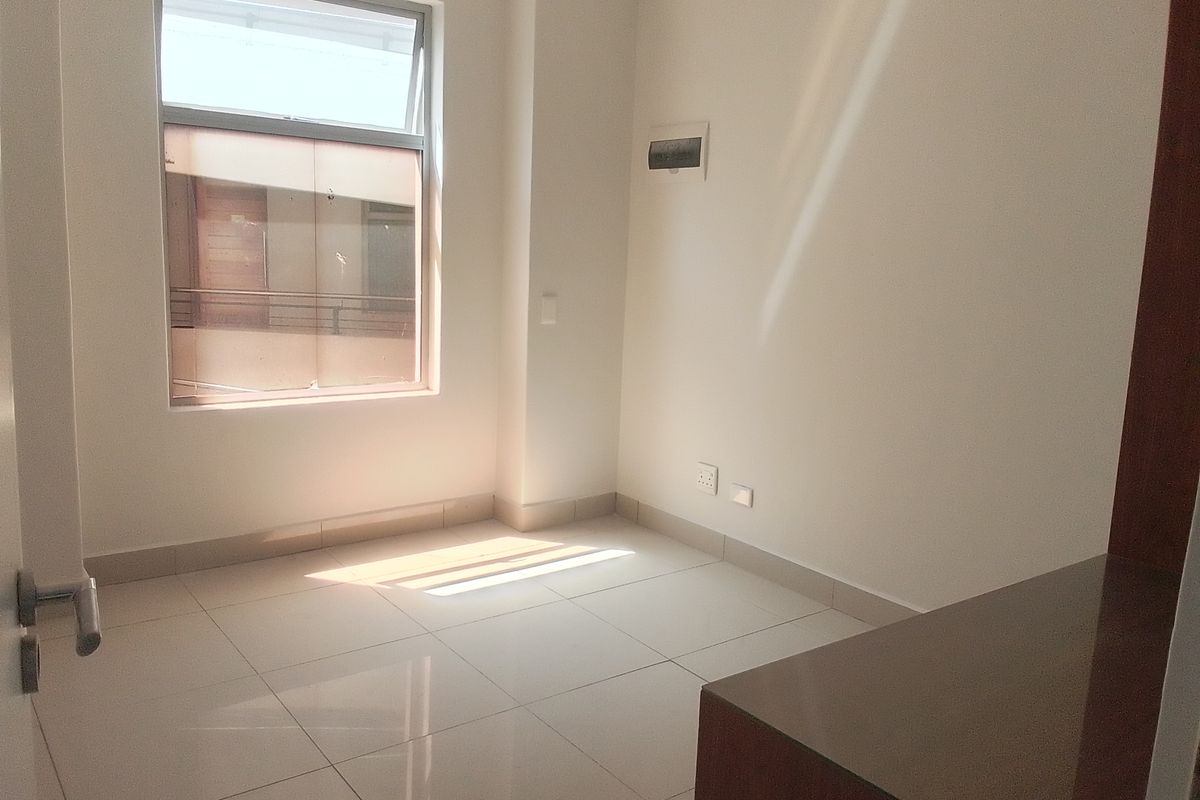 A bright, empty bedroom featuring neutral tiled flooring, a large window, and clean wall finishes, ready for personalization.