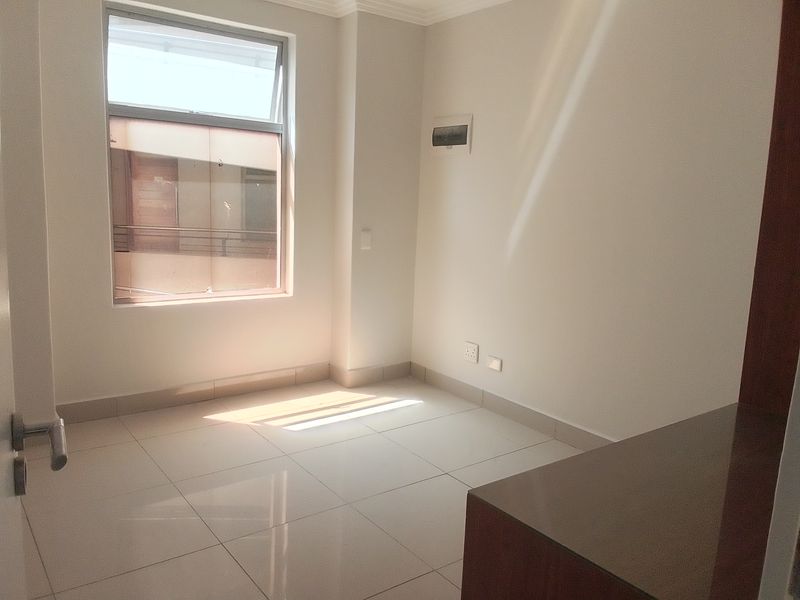 A bright, empty bedroom featuring neutral tiled flooring, a large window, and clean wall finishes, ready for personalization.