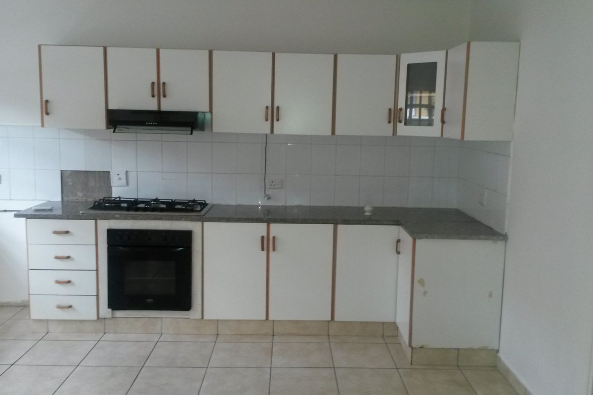 A functional kitchen featuring white built-in cabinetry, a gas hob, an integrated oven, and tiled flooring, offering a clean and practical workspace.