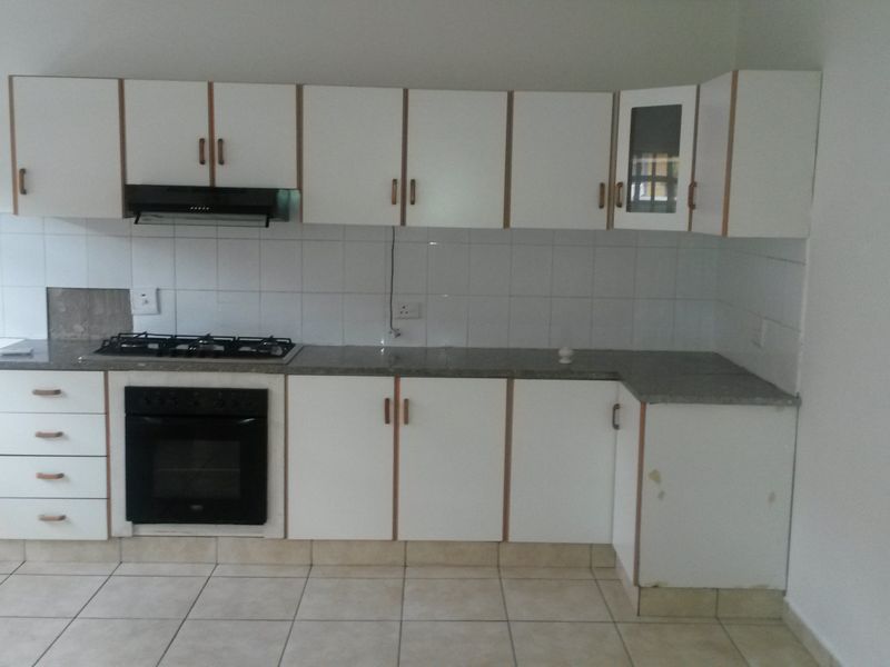 A functional kitchen featuring white built-in cabinetry, a gas hob, an integrated oven, and tiled flooring, offering a clean and practical workspace.