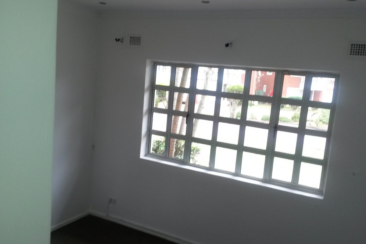 A vacant bedroom featuring a grid-pattern window, recessed ceiling lighting, and ventilation grilles, offering a clean and neutral space ready for personalization.