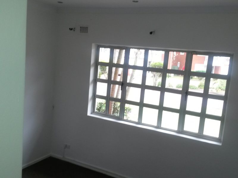 A vacant bedroom featuring a grid-pattern window, recessed ceiling lighting, and ventilation grilles, offering a clean and neutral space ready for personalization.