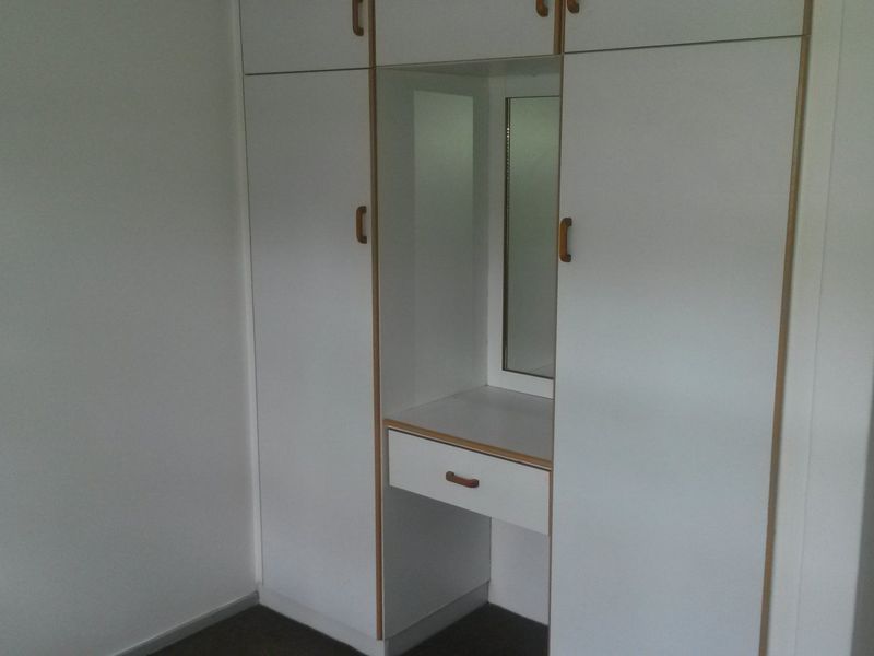 A bedroom featuring built-in white cabinetry with an integrated vanity and mirror, providing ample storage space.