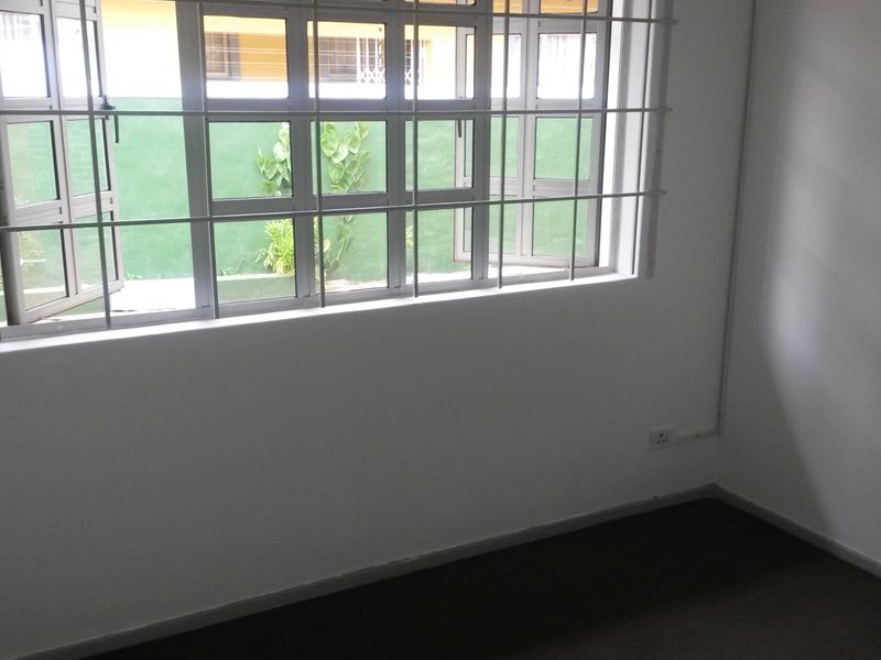 A clean, empty bedroom featuring white walls, dark flooring, and large windows fitted with security bars.