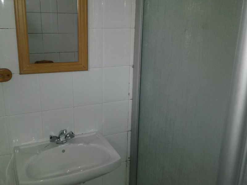A functional bathroom featuring a wall-mounted basin with chrome tapware and a shower enclosure with tiled walls.