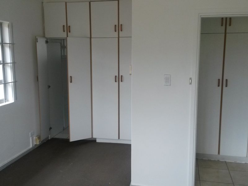 An empty bedroom featuring built-in cupboards, security bars on the window, and a combination of carpeted and tiled flooring.