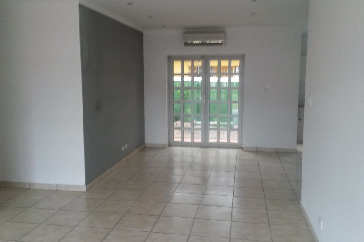 An empty, open-plan living area featuring neutral tiled flooring, a feature wall, and glass double doors leading to the exterior.
