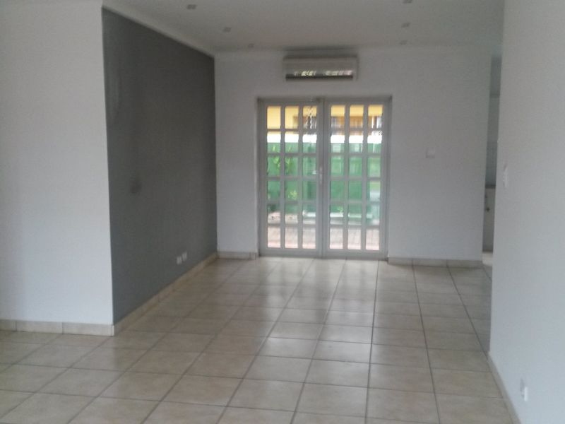 An empty, open-plan living area featuring neutral tiled flooring, a feature wall, and glass double doors leading to the exterior.