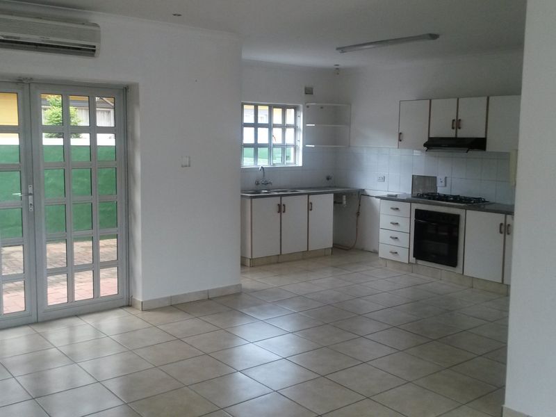 Spacious open-plan kitchen and living area featuring tiled floors, built-in cabinetry, gas hob, oven, and direct access to the exterior through french doors.