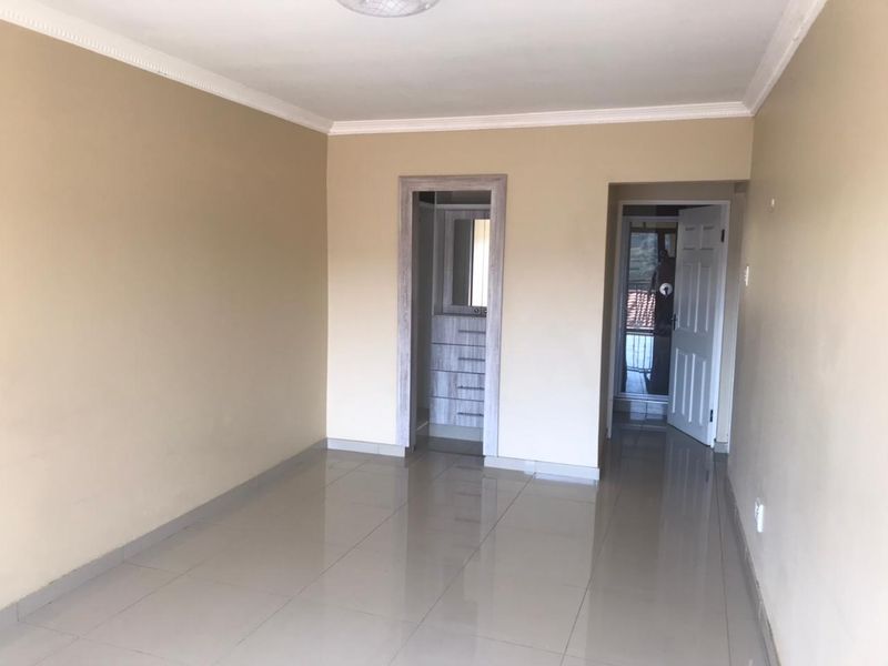 A clean, empty bedroom featuring neutral wall tones, tiled flooring, decorative cornicing, and a built-in vanity or storage area.
