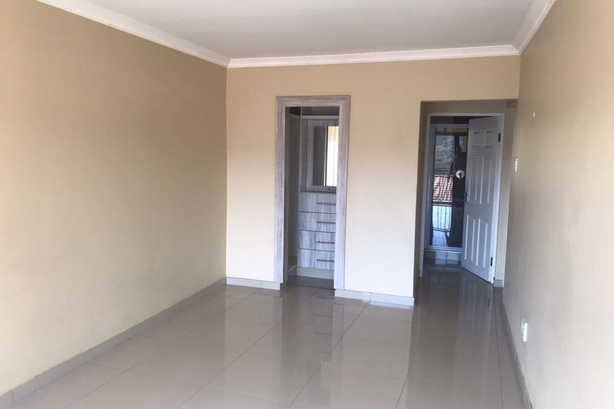 A clean, empty bedroom featuring neutral wall tones, tiled flooring, decorative cornicing, and a built-in vanity or storage area.