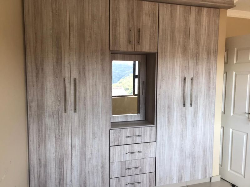 A bedroom featuring modern, light wood-grain built-in cupboards with an integrated vanity and drawer unit.