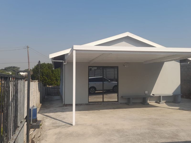 A neat front exterior view featuring a covered carport, concrete driveway, and a sliding glass door entrance.