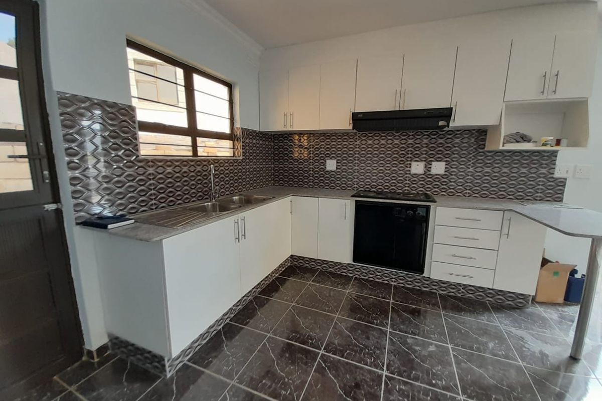 A clean, functional kitchen featuring white cabinetry, dark patterned tiled backsplash, built-in oven and hob, and dark marble-effect floor tiles.