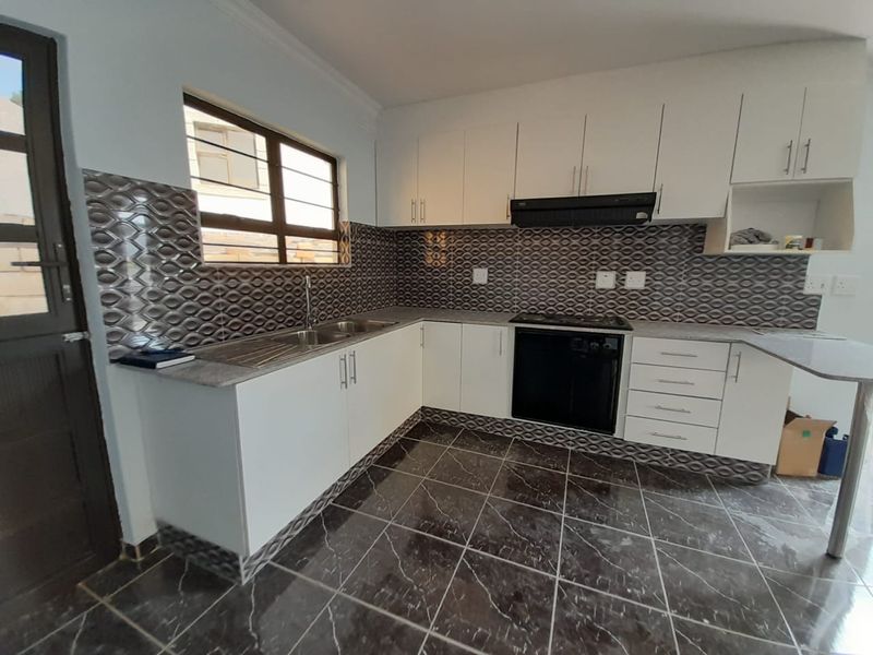 A clean, functional kitchen featuring white cabinetry, dark patterned tiled backsplash, built-in oven and hob, and dark marble-effect floor tiles.