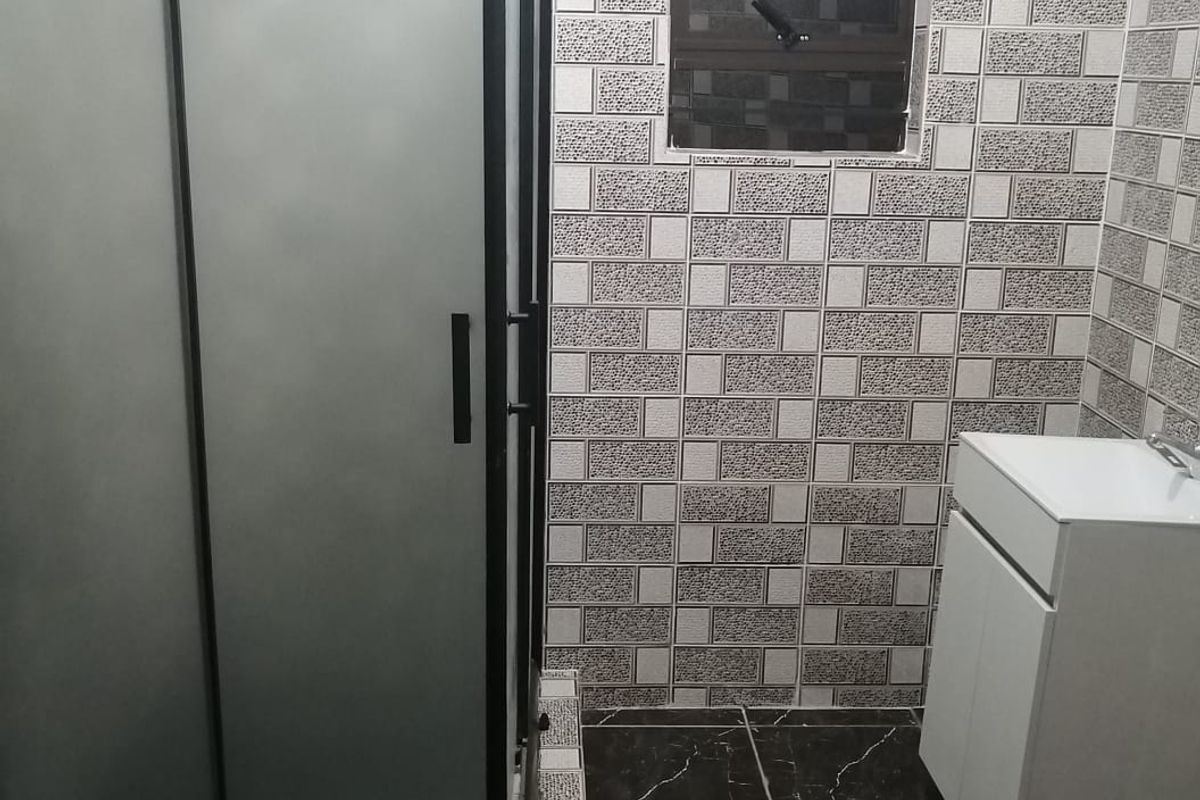 A modern bathroom featuring a glass shower enclosure, a white vanity cabinet with a basin, and contrasting tiled walls and flooring.
